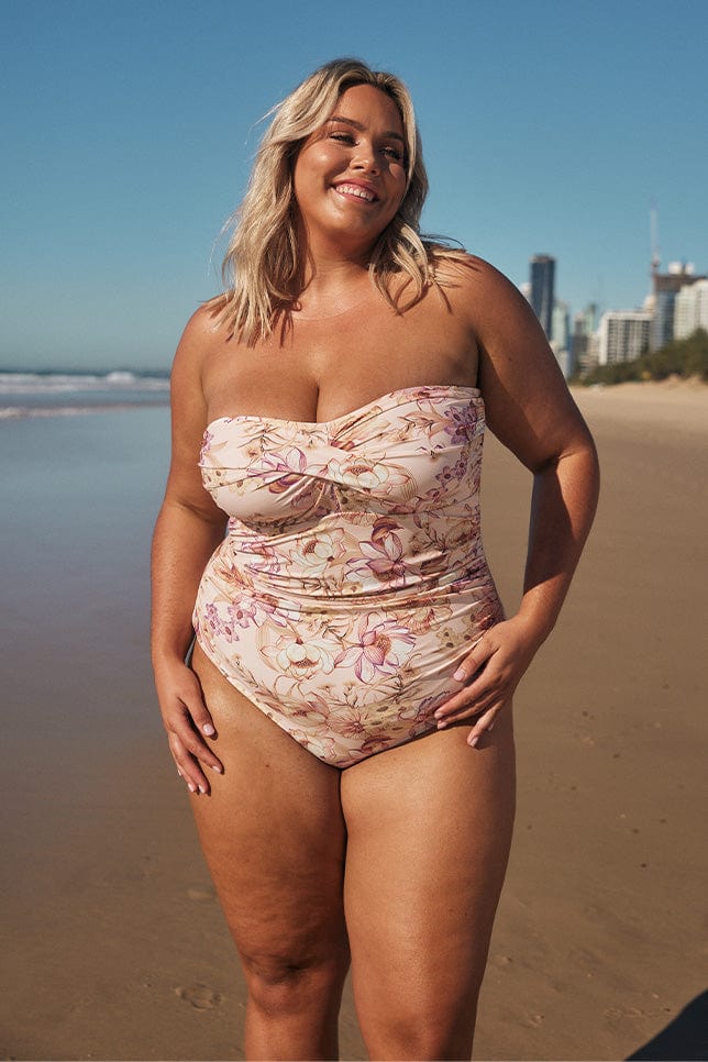Blonde model wearing light pink floral strapless swimsuit on beach