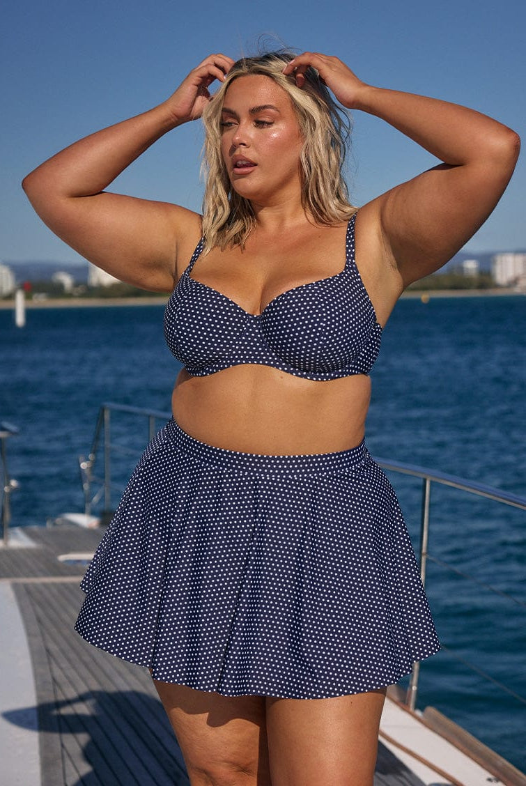 Woman wearing a navy polka dot bikini set on a boat with water and sky in the background