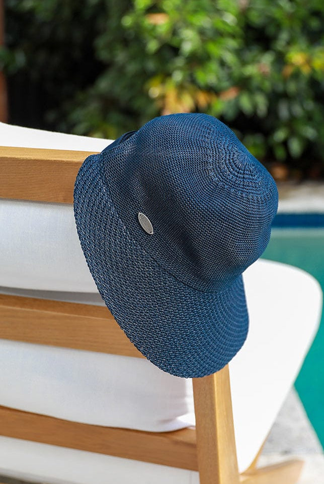 image of navy straw wide brim hat laying beside a pool on a natural and white beach chair