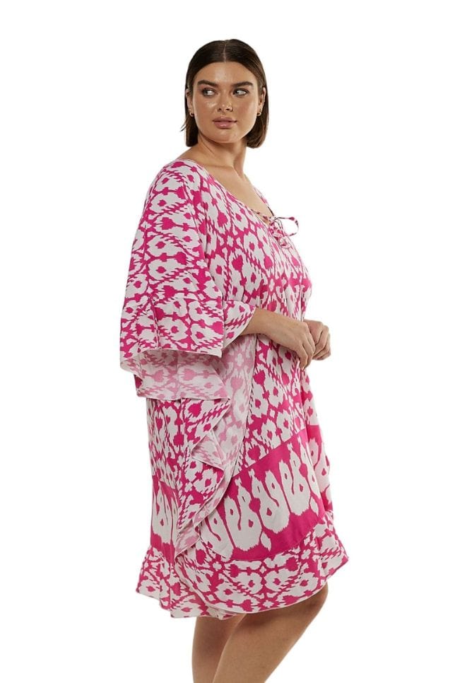 Side of brunette model wearing pink and white patterned beach kaftan