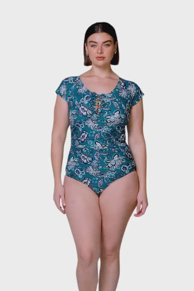brunette model wearing cap sleeve one piece with tie front detail in deep floral teal