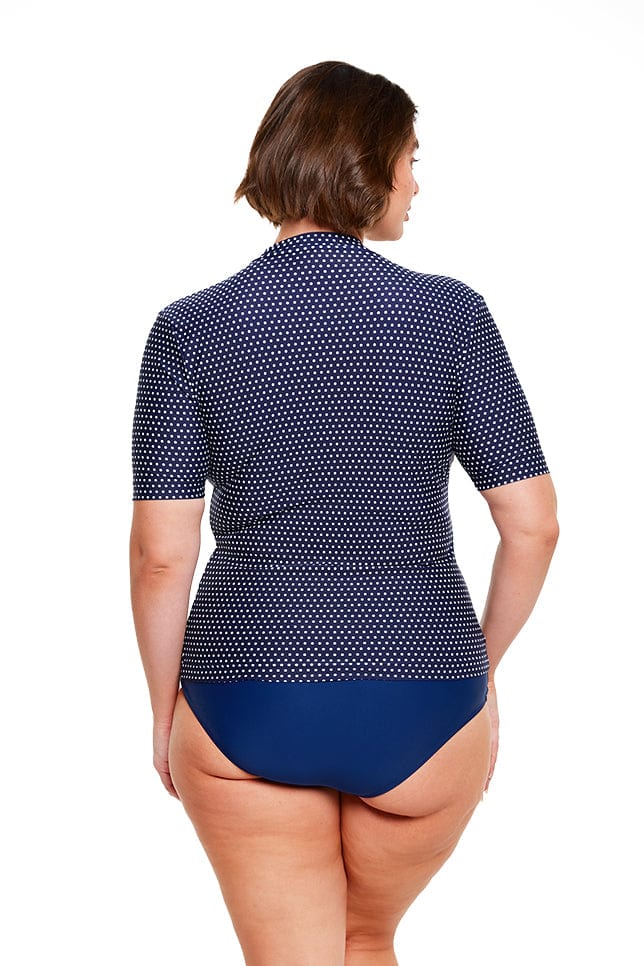 brunette model wears navy and white dots short sleeve rash vest with full front zip