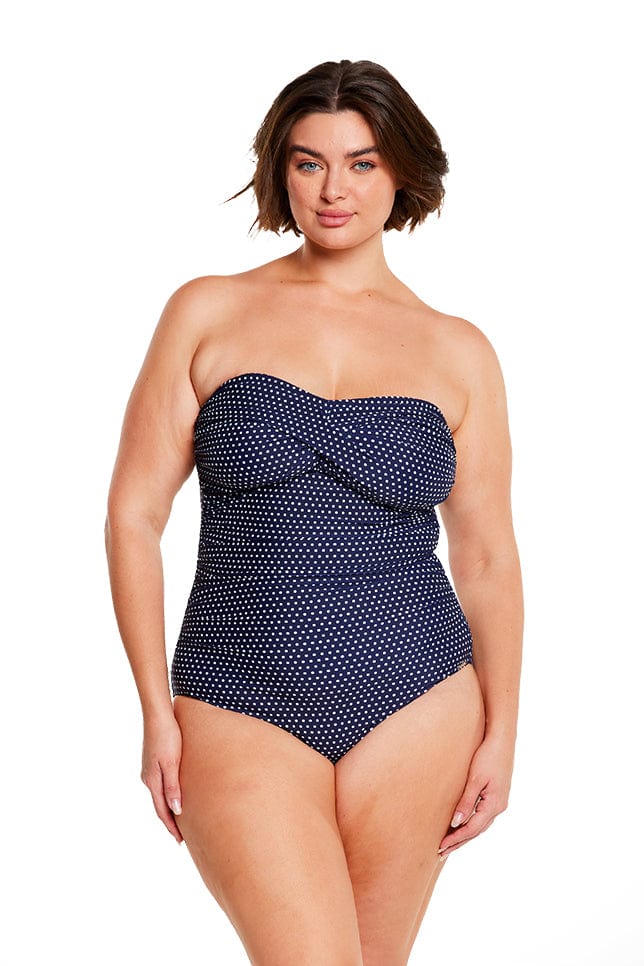 Brunette model wears strapless bandeau one piece with navy and white dots