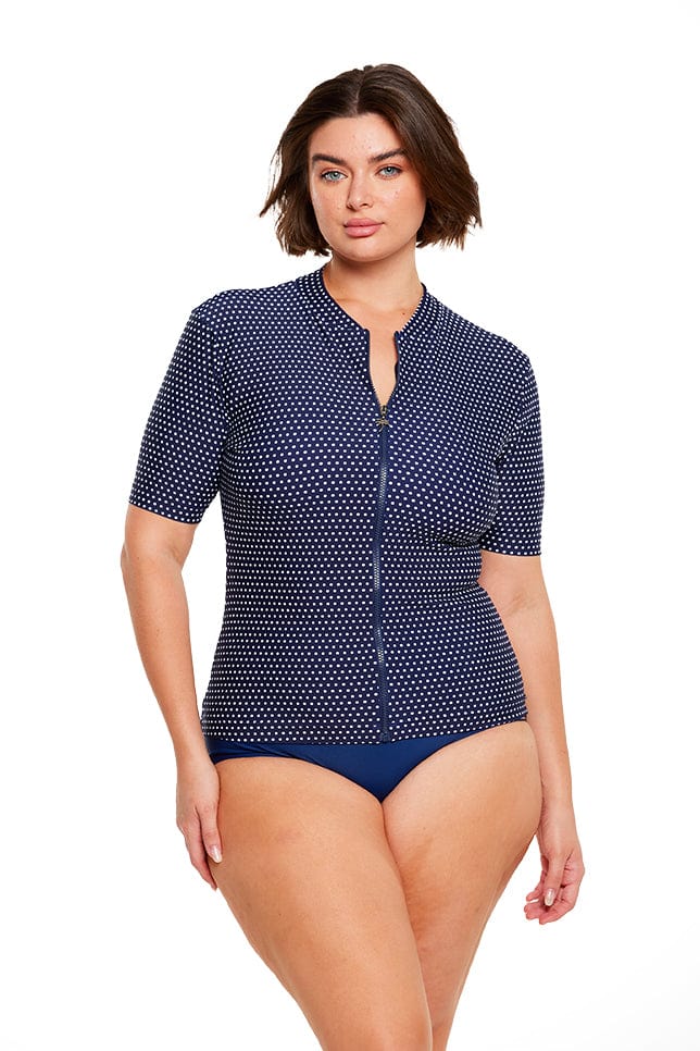 Brunette model wears navy polkadot full zip front short sleeve rash vest