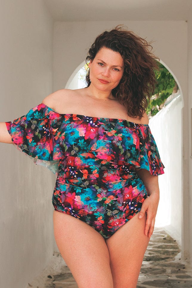 brunette plus size model wearing off the shoulder one piece in a vibrant floral print