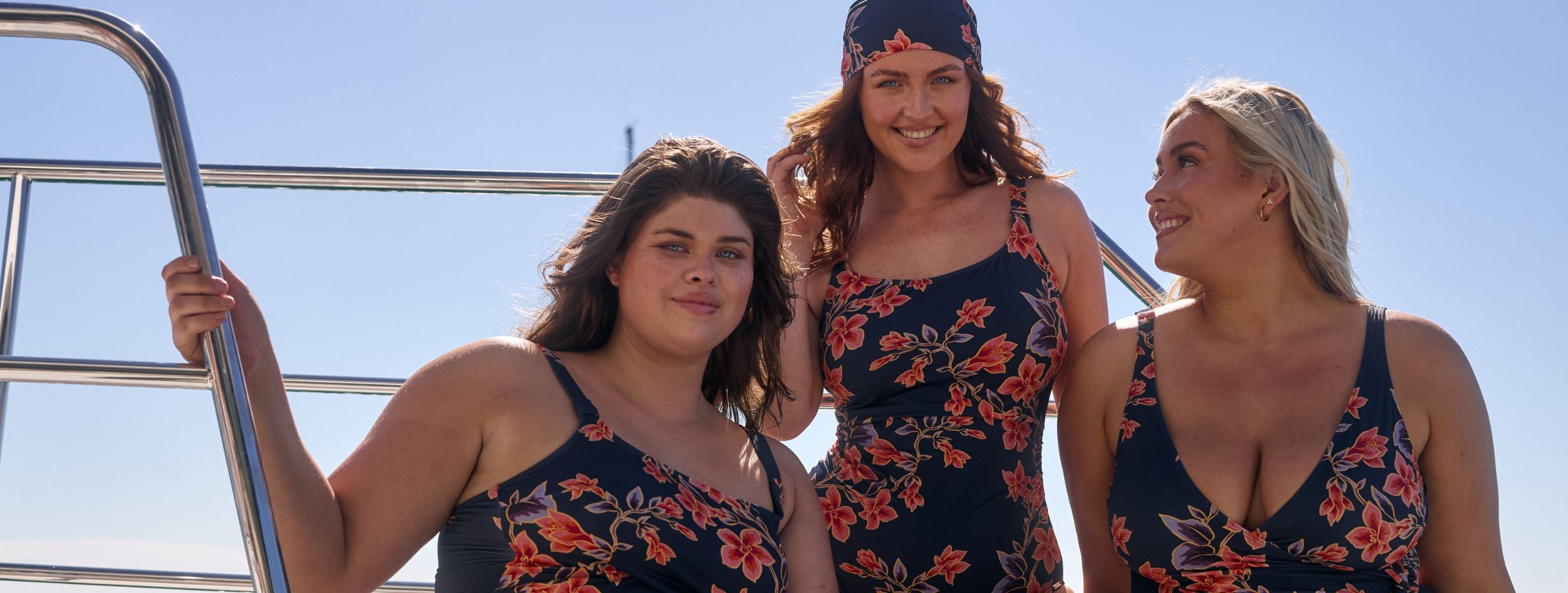 3 women pose on a boat wearing floral swimsuits