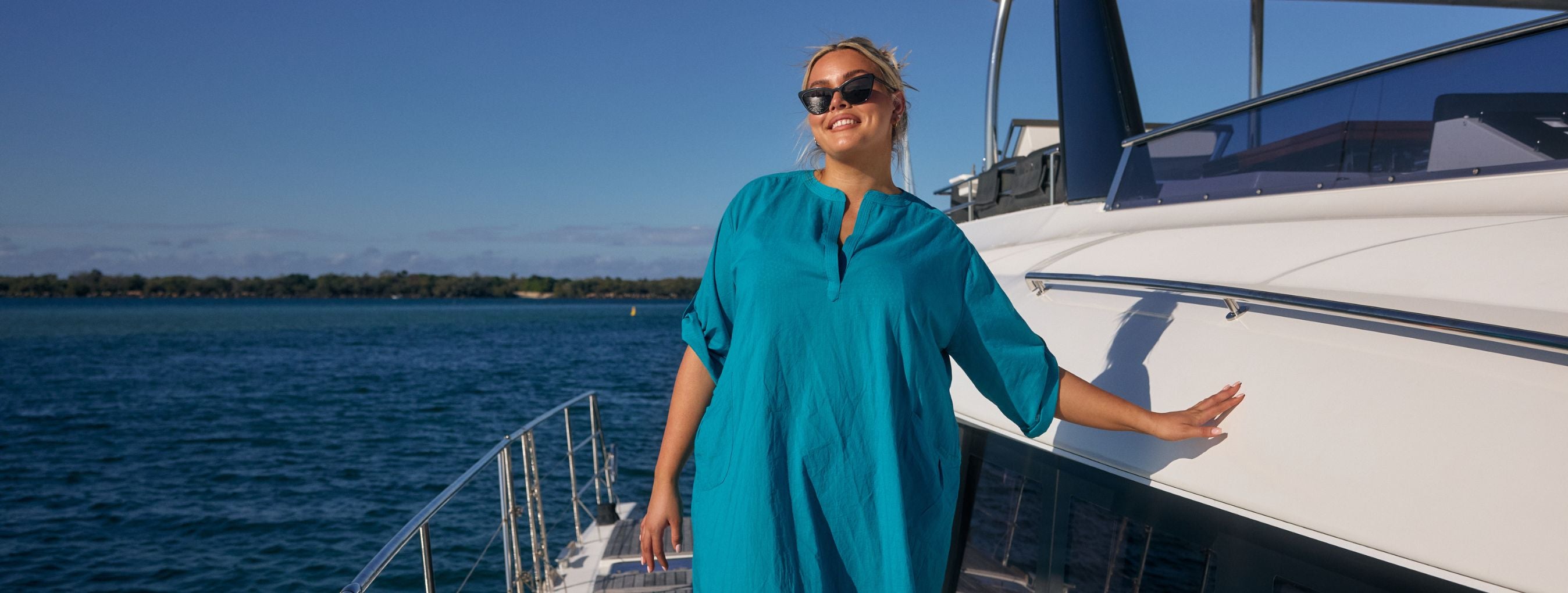 Woman with blonde hair poses on a boat wearing a teal cotton beach cover up