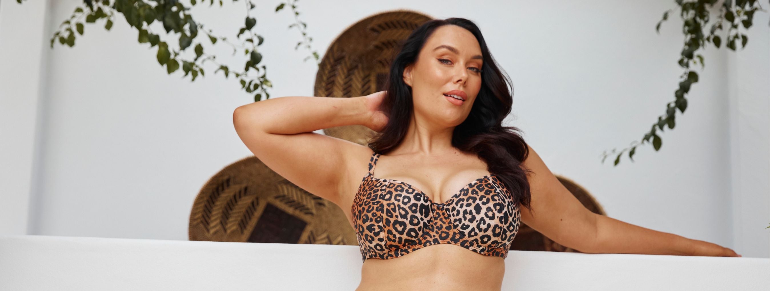 Woman with long brown hair poses against a white wall wearing leopard print underwire bikini top 