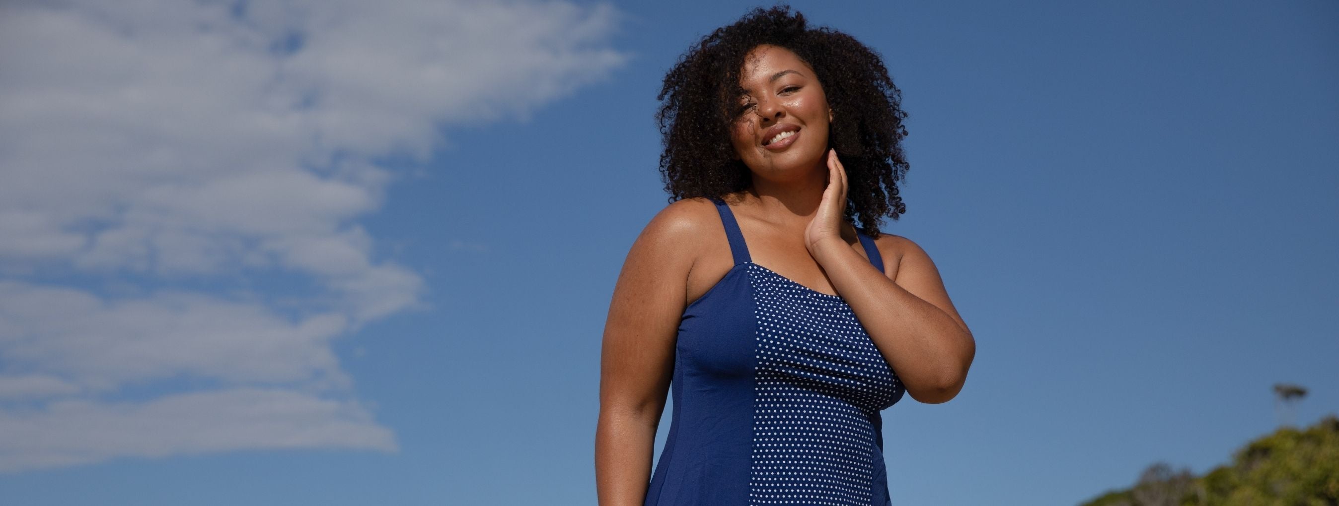 Brunette model wears navy and white dots wide strap swim dress