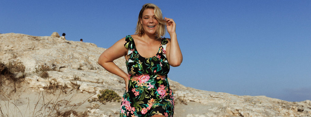 Woman with short blonde hair wears black, pink, and green floral swim dress. 