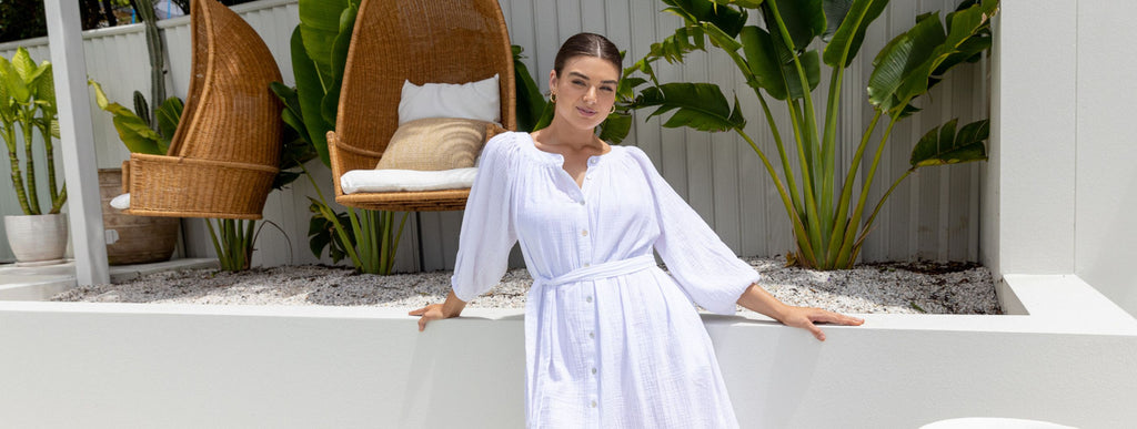 Woman with slicked back brown hair wears white cotton button up beach dress