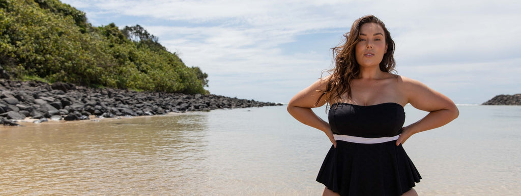 Brunette model poses on the beach wearing Acapulco black peplum strapless tankini top