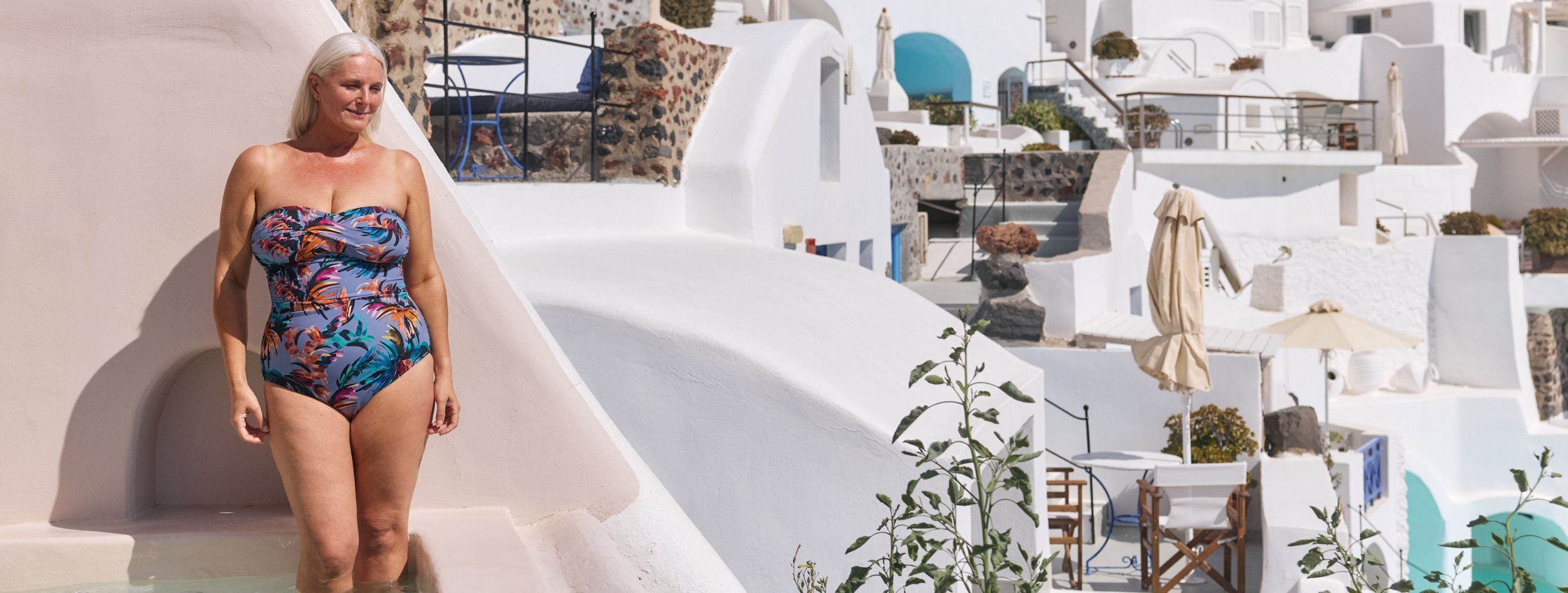 Woman poses on a terrace in Santorini wearing a tropical print strapless one piece swimsuit