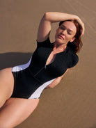 Woman in a black and white swimsuit standing on sand