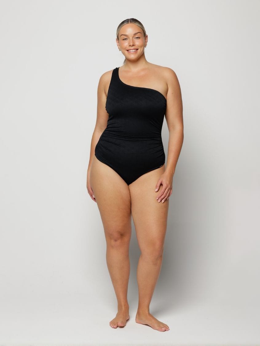 Woman wearing a black one-shoulder swimsuit on a white background