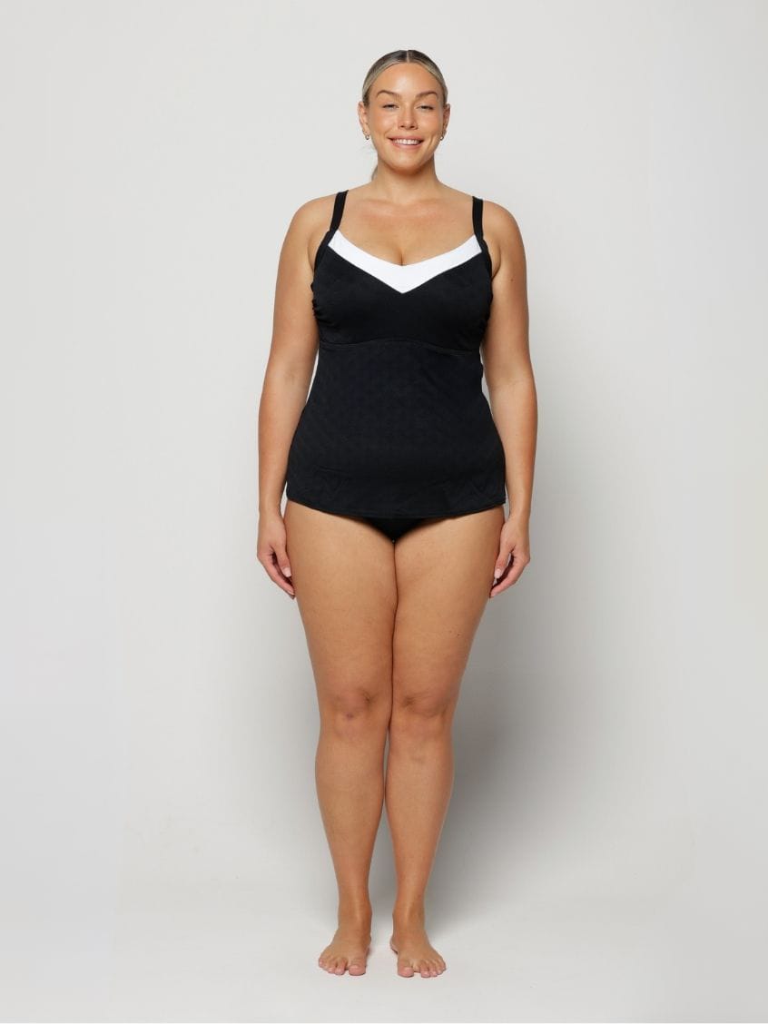 Woman wearing a black swimsuit with white accents on a plain background