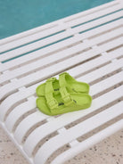 kids lime green sandals on a pool chair beside a pool.
