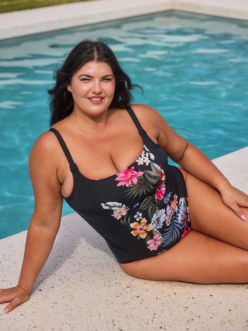Brunette model wears black floral pool proof scoop beck one piece by the pool