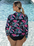 Woman wearing a colorful leaf-patterned rash guard by a pool.