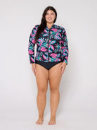 Woman wearing a colorful floral rash guard and black swimsuit bottom on a white background
