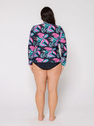 Person wearing a colorful tropical print long-sleeve shirt over a black swimsuit on a white background