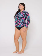 Woman wearing a colorful long-sleeve rash guard and black swimsuit bottoms on a white background