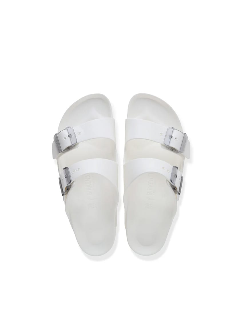 A pair of white double-strap slide sandals with silver buckle closures, photographed from a top-down perspective on a clean white background.