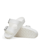 A pair of white double-strap slide sandals with textured soles and small silver buckle details, shown on a clean white background.