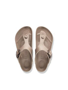 A pair of light taupe/beige thong sandals with dark metal buckles, shown from a top-down view on a white background.
