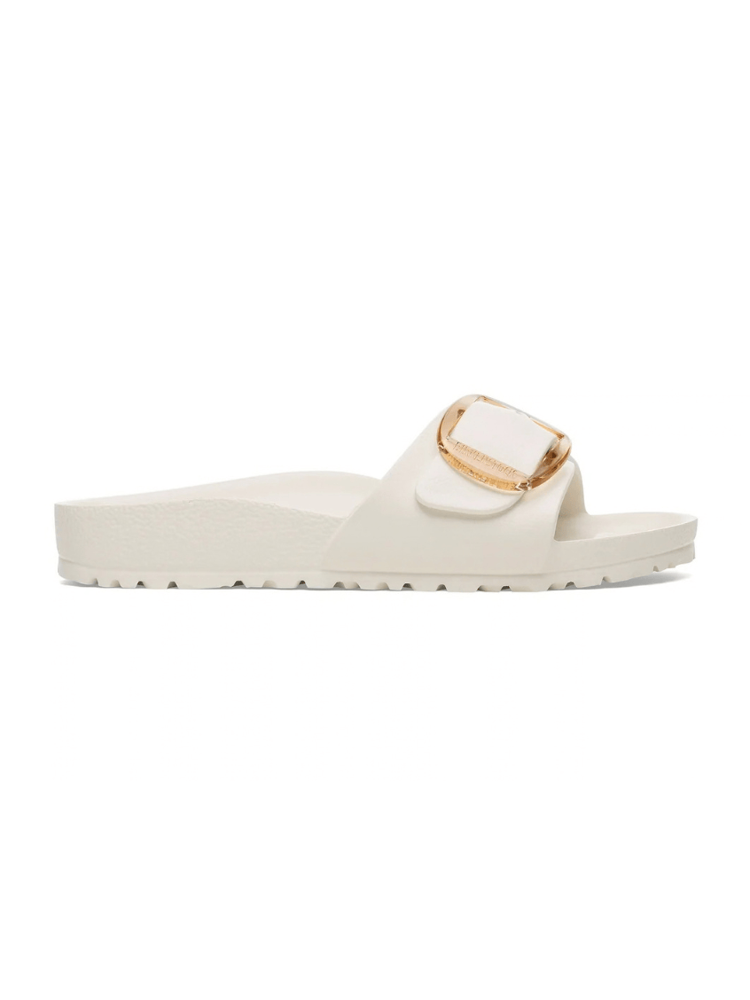 An off-white slide sandal with a wide strap featuring a gold-tone buckle closure, shown from a side profile on a white background.