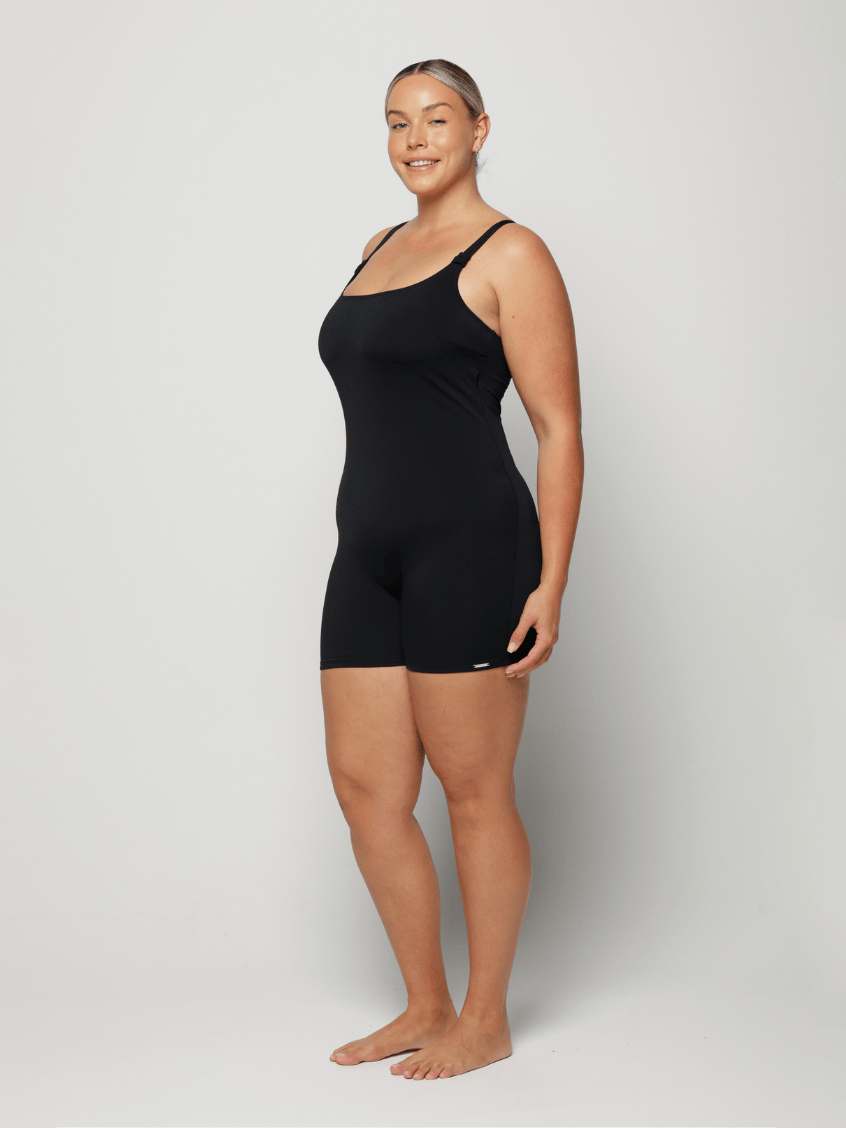 Woman wearing a black boyleg one piece against a white background
