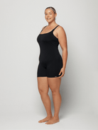 Woman wearing a black boyleg one piece against a white background