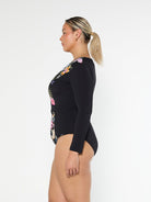 Blonde model showing the side of modest black long sleeve one piece in pool proof fabric