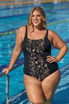 Model wearing black floral tank one piece at public pool