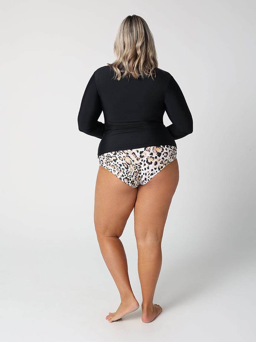 Person wearing a black long-sleeve top and leopard print underwear on a white background