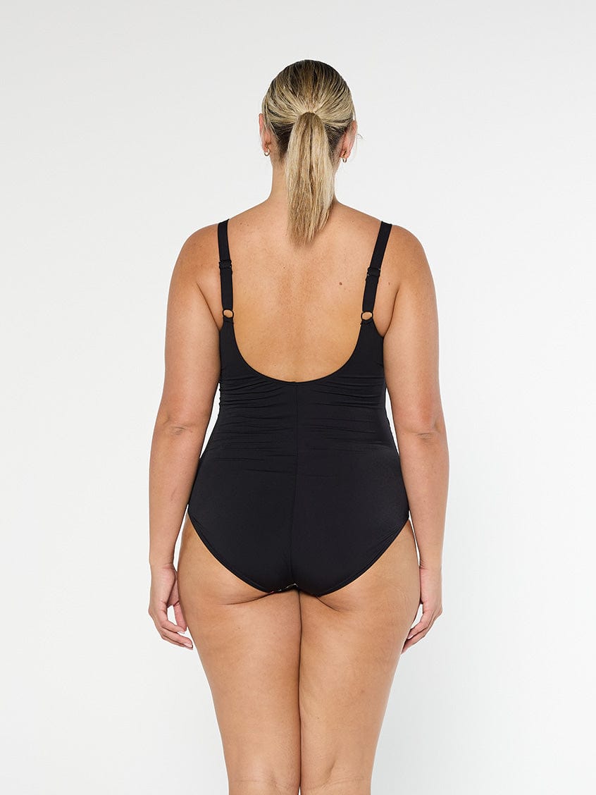Blonde model shows the back of black pool proof one piece with low scoop back and adjustable straps