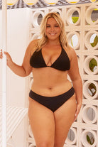 Blonde model wearing black mid rise bikini bottoms and bikini top