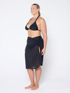 Woman wearing a black bikini and matching sarong on a white background