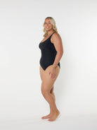model standing in front of a white wall wearing a black one piece swimsuit