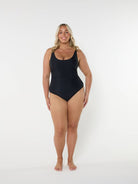 model standing in front of a white wall wearing a black one piece swimsuit