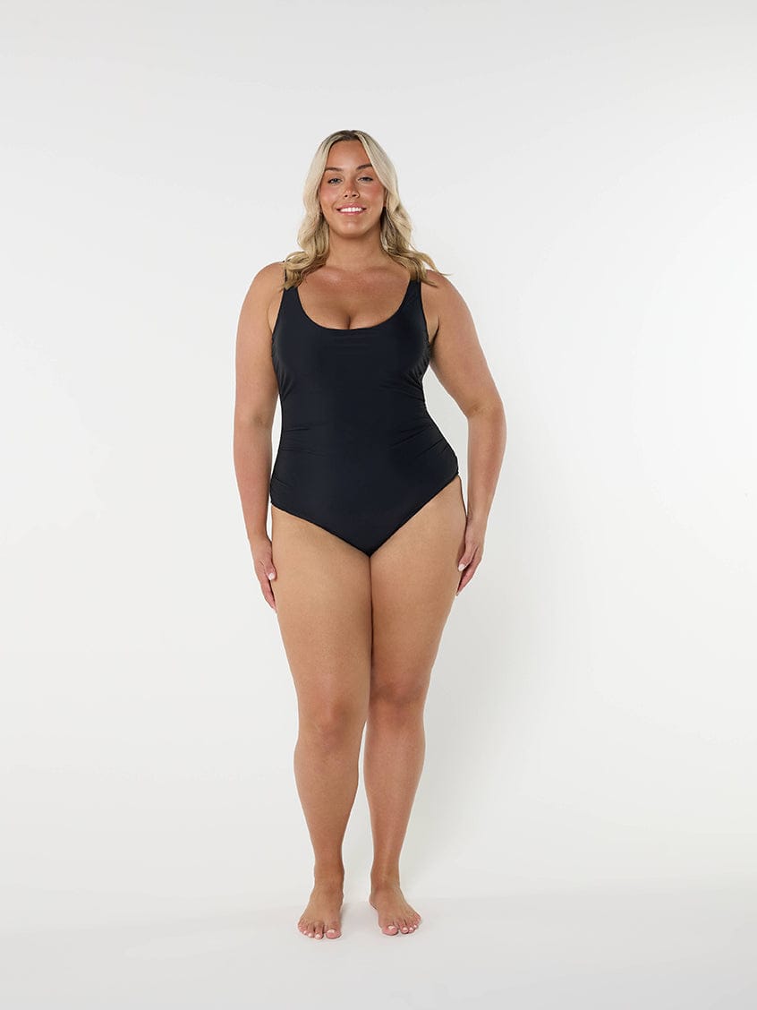 model standing in front of a white wall wearing a black one piece swimsuit