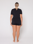 Person wearing a black boyleg one piece with zip front against a white background