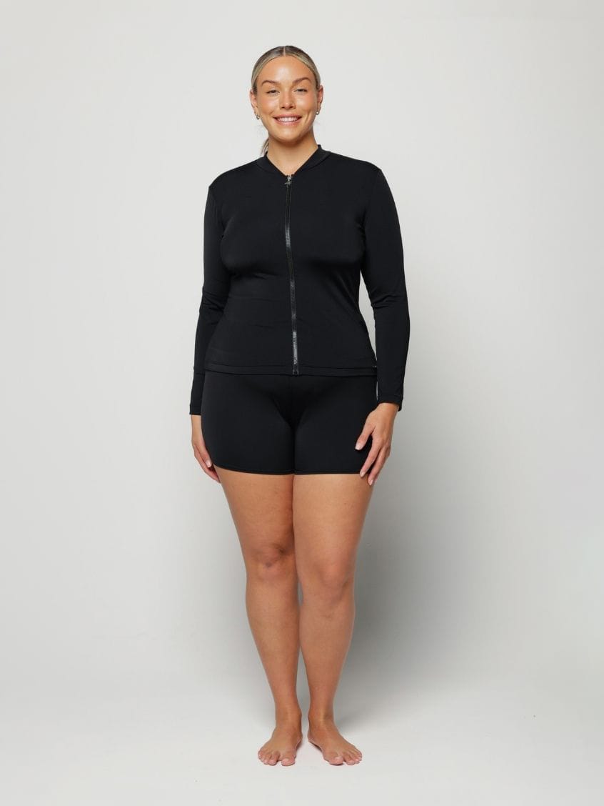 Woman wearing a black long-sleeve rash vest top with a zip and white background behind her