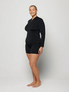 Woman wearing a black long-sleeve rash vest top with a zip and white background behind her