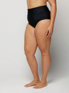 Woman wearing black high-waisted bikini bottoms on a plain background