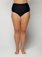 Woman wearing black high-waisted bikini bottoms on a plain background