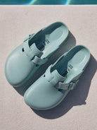 Pair of light blue clogs on a diving board with a pool in the background