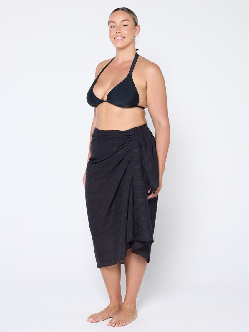 Woman wearing a black bikini and matching sarong on a white background