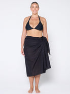 Woman wearing a black bikini and black sarong on a white background