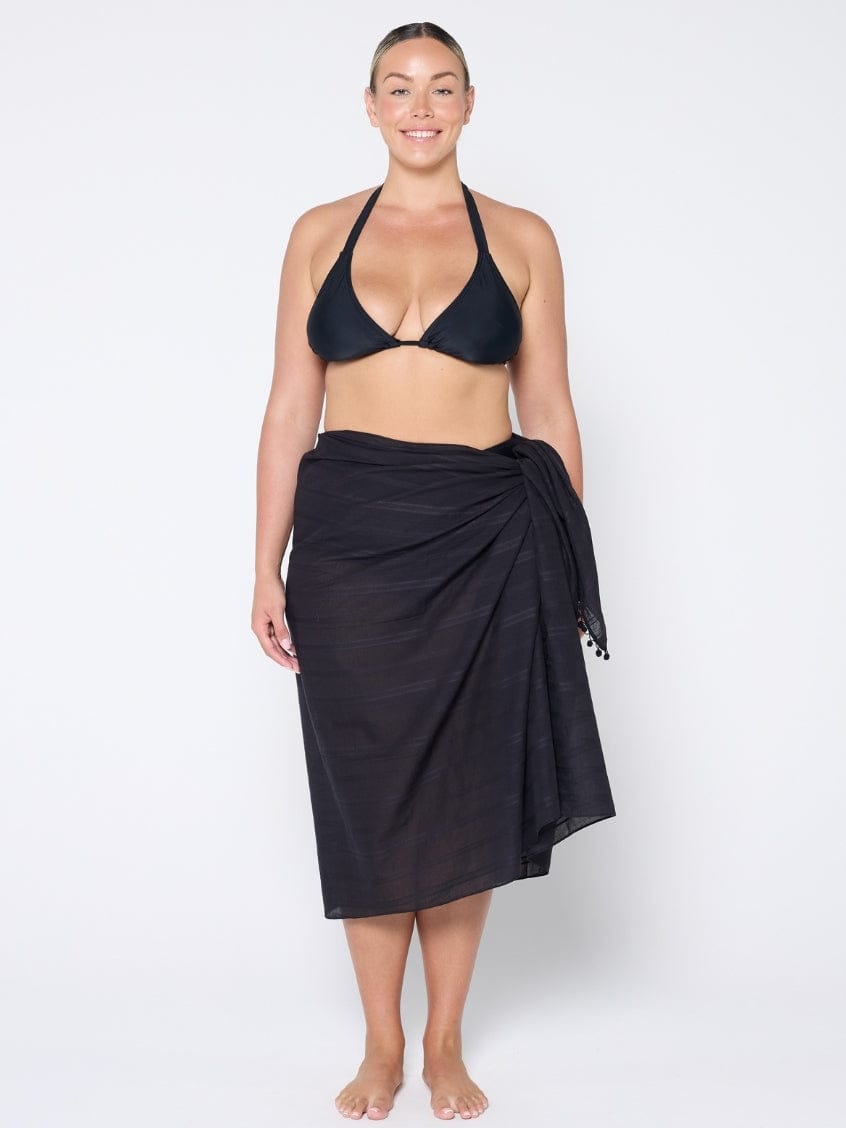 Woman wearing a black bikini and black sarong on a white background